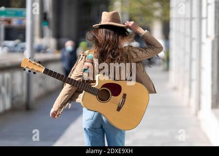 Jeune femme avec guitare portant un chapeau marchant sur le sentier dans ville Banque D'Images