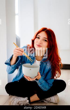 Femme d'affaires souriante mangeant des nouilles au bureau Banque D'Images