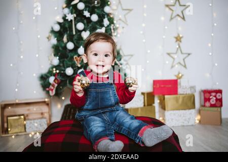 Bébé garçon heureux jouant avec la boule tout en étant assis à la maison Pendant Noël Banque D'Images