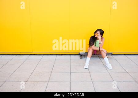 Portrait d'une belle fille assise seule à bord long devant le jaune mur Banque D'Images