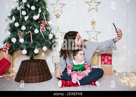 Mère prenant selfie avec son fils par téléphone portable pendant qu'elle est assise À la maison pendant Noël Banque D'Images