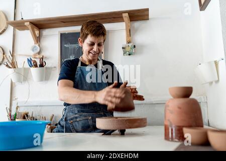 Femme souriante potter travaillant avec de l'argile brune au magasin de céramique Banque D'Images