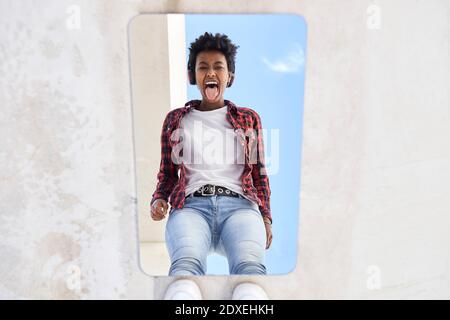 Jeune femme afro joyeuse qui colle à la langue tout en réfléchissant miroir Banque D'Images