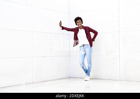 Jeune femme hipster souriante écoutant de la musique tout en s'appuyant sur le blanc mur Banque D'Images