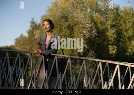 Femme entrepreneur se penchant sur la main courante tout en se tenant au-dessus de la passerelle pendant automne Banque D'Images