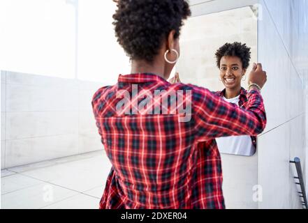 Jeune femme afro souriante tenant le miroir contre le mur Banque D'Images