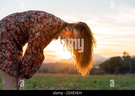 Jeune femme souriante aux cheveux bruns qui se replient au coucher du soleil Banque D'Images