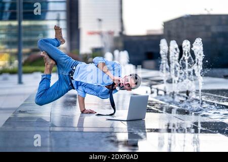 Homme d'affaires avec un ordinateur portable buvant du café tout en faisant la main près de la fontaine sur le sentier Banque D'Images