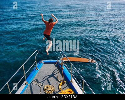 Homme aventureux sautant sur le pont du bateau pour faire du surf jour ensoleillé Banque D'Images