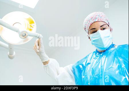 Médecin dentaire réglant la lampe électrique éclairée pendant qu'il se trouve à la clinique Pendant Covid-19 Banque D'Images