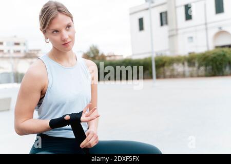 Femme confiante qui regarde loin tout en nouant le wrap de boxe à la main à l'extérieur Banque D'Images