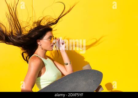 Portrait de la jeune belle femme qui jette les cheveux devant mur jaune avec planche à repasser à la main Banque D'Images