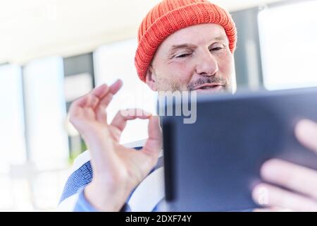 Homme mûr montrant le signe de main OK tout en parlant à la vidéo appelez sur une tablette numérique à la maison Banque D'Images