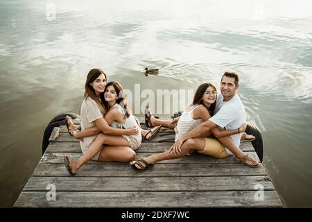 Filles embrassant mère et père tout en étant assis sur la jetée contre lac Banque D'Images