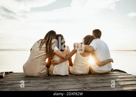 Les parents et les enfants avec les armes autour de s'asseoir sur la jetée regardant à vue contre le ciel Banque D'Images