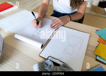 Jeune femme designer de mode esquissant le design dans le livre au studio Banque D'Images