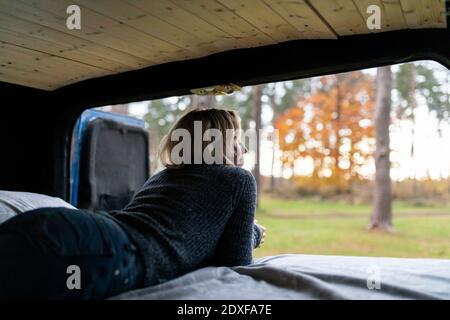 Femme confortable regardant à l'extérieur tout en étant allongé sur le lit dans la cabine de camping fourgonnette Banque D'Images