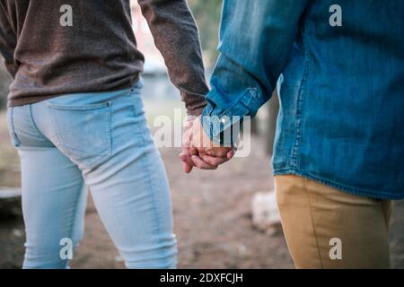 Couple gay tenant les mains en marchant dans le parc public Banque D'Images