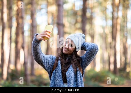 Femme souriante, main derrière la tête, prenant le selfie tout en étant debout Dans la forêt de Cannock Chase Banque D'Images