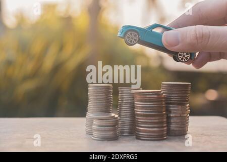 Main tenant les pièces de monnaie modèle de voiture pile sur la table en bois Finance Concept d'assurance et de transport Banque D'Images