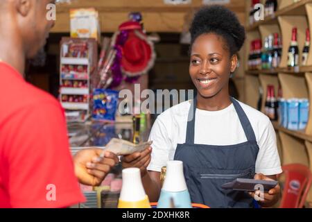 une femme de boutique africaine souriant tout en collectant de l'argent auprès d'un client Banque D'Images