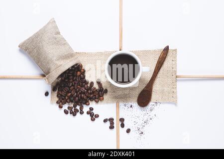 tasse de café blanc, grains de café déversés du sac, cuillère en bois avec café sur fond blanc. Vue de dessus. Banque D'Images