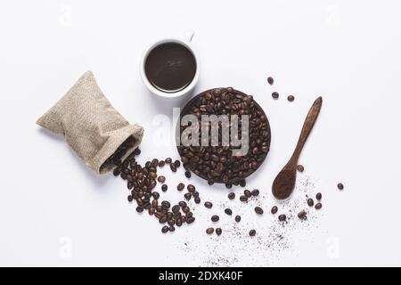 tasse de café blanc, grains de café déversés du sac, cuillère en bois avec café sur fond blanc. Vue de dessus. Banque D'Images