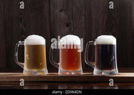 Trois types de bière froide en cruches sur base en bois. Banque D'Images