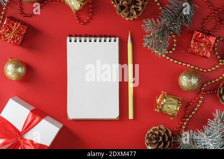 Bloc-notes et crayon pour écrire des voeux et des cadeaux pour le nouvel an et Noël autour des décorations d'arbre de Noël sur un fond rouge. Nouvel an moo Banque D'Images
