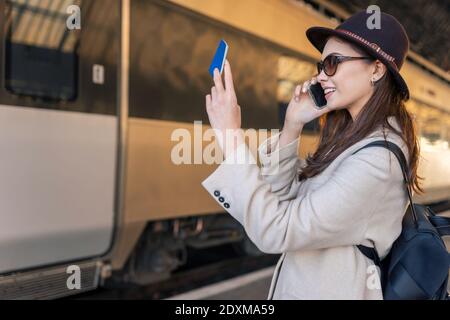 La femme voyageur regarde dans le passeport et parle sur son téléphone portable en se tenant sur la plate-forme de la gare et en attente de son train Banque D'Images