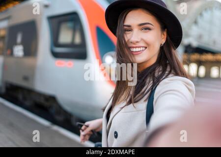 Une jolie fille touriste prend selfie à la gare contre le contexte de la locomotive Banque D'Images