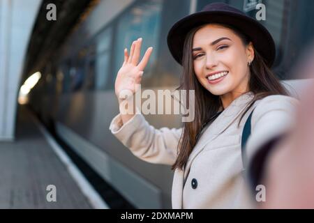 Jolie fille touriste prend selfie à la gare de chemin de fer contre le fond de la locomotive. Une fille parle lors d'un appel vidéo Banque D'Images