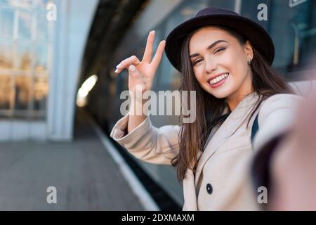 Jolie fille touriste prend selfie à la gare de chemin de fer contre le fond de la locomotive. Une fille parle lors d'un appel vidéo Banque D'Images