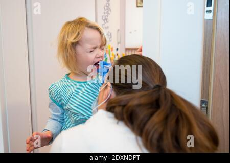 Fille blonde ayant un écouvillon oropharyngé inséré pour la détection de covid 19. Banque D'Images