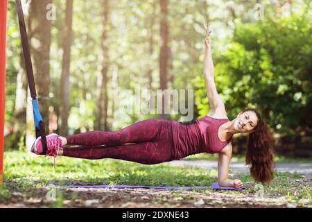 Une jeune femme effectue un exercice de planche latérale sur une machine suspendue attachée à une barre horizontale dans un parc. Banque D'Images