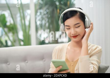 Smiling girl détente à la maison, elle est en train d'écouter de la musique à l'aide d'un smartphone et portant un casque blanc Banque D'Images