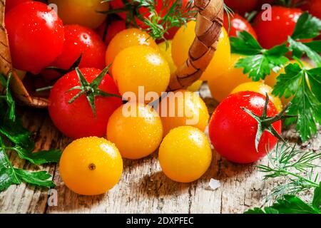 Les tomates cerises rouges et jaunes sortent d'un panier en osier, fond en bois vintage, style campagnard, mise au point sélective Banque D'Images