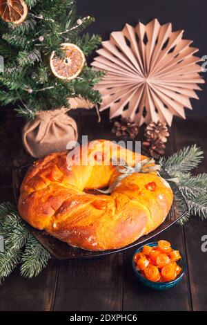 Pain de Noël fait maison dans une forme de couronne de l'Avent de pâte de levure avec des fruits confits d'orange sur fond d'arbre de Noël. Banque D'Images