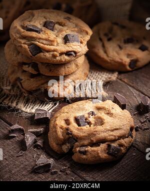 Gros plan d'un cookie de chocolat avec des cookies en arrière-plan et des morceaux de chocolat sur une table rustique en bois Banque D'Images