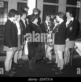 Années 1960, historiques, grands sourires tout autour comme une équipe de hockey d'écolières dans leurs bottes boueuses et blazers sont présentés avec le trophée gagnant par une dame dans un manteau de fourrure, Fife, Écosse, Royaume-Uni. Banque D'Images