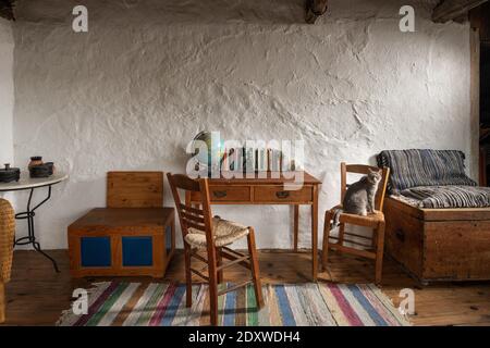 Vue avant de l'intérieur d'une chambre vintage dans une maison de campagne traditionnelle du village. Mobilier artisanal ancien, bureau d'école, chaises en bois, coffre sur stuc wa Banque D'Images