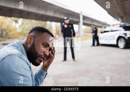 A perturbé la victime afro-américaine en regardant à l'écart près des policiers et voiture sur fond flou dans la rue urbaine Banque D'Images