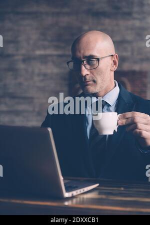 En prenant une pause café et en regardant la correspondance d'affaires, un homme d'affaires tient une tasse de café dans sa main et regarde dans l'écran d'ordinateur portable Banque D'Images