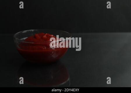 pâte de sauce tomate rouge dans un bol de sauce en verre sur fond noir copier l'espace pour le texte. Banque D'Images