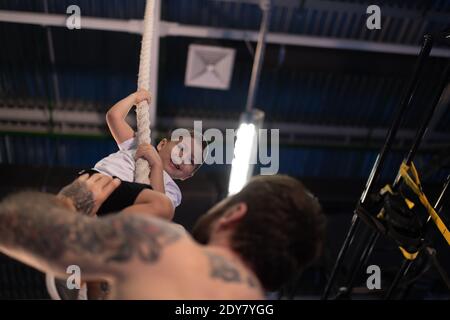 De dessous l'homme tatoué soutenant le garçon ravi tout en enseignant son pour monter la corde contre le plafond dans la salle de gym Banque D'Images