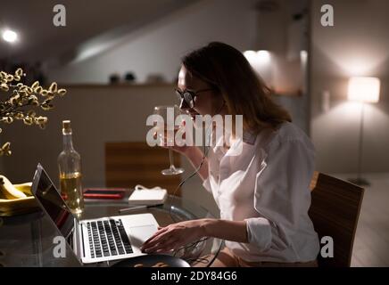 Vue latérale d'une jeune femme entrepreneure gaie en tenue habillée et des verres passant le soir à la maison dans l'isolement mais rester connecté avec Banque D'Images