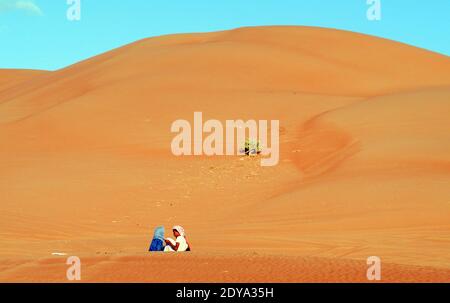 Des filles bédouines assises près des dunes de sable de Wahiba en Oman. Banque D'Images