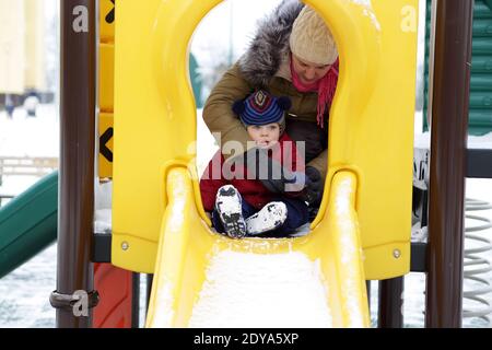 Tout-petit sur un toboggan à l'aire de jeux en hiver Banque D'Images