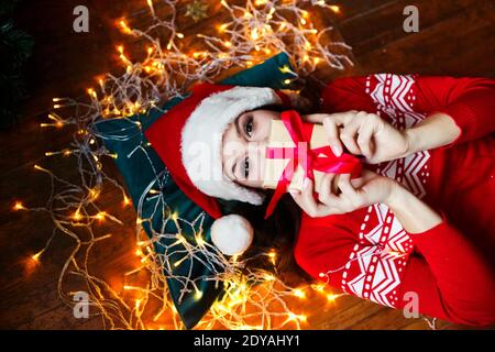 Portrait d'une femme mignonne couché sur le sol et tenant le présent dans la chambre avec des décorations de noël Banque D'Images