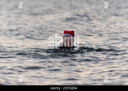 Southend on Sea, Essex, Royaume-Uni. 25 décembre 2020. Le jour de Noël à Southend a été froid mais lumineux, avec des températures juste au-dessus de zéro. La température de l'eau d'environ sept degrés n'a pas mis les nageurs d'eau froide de prendre à l'estuaire de la Tamise. Une femme nageant dans un chapeau de père Noël Banque D'Images